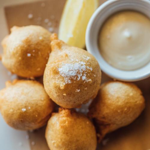 Golden, crispy fritters topped with salt, served with a lemon wedge and a small bowl of dipping sauce.