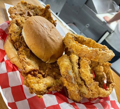 A basket with a fried chicken sandwich and crispy onion rings on a red and white checkered paper.