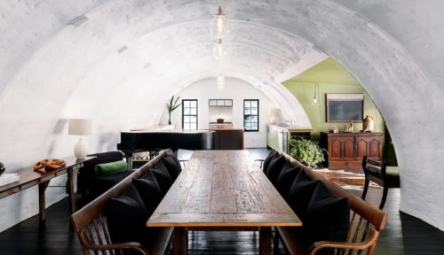 A spacious, modern dining area with a long wooden table, curved white walls, and a piano in the background.