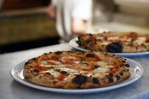 Two freshly baked pizzas on white plates, featuring melted cheese and a slightly charred crust, on a marble countertop.