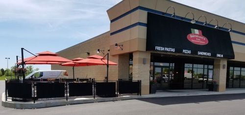 Exterior of a restaurant with outdoor seating, featuring umbrellas and a delivery van parked nearby. Clear blue sky above.
