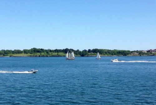 Three boats sail on a calm blue waterway, with green trees lining the shore under a clear blue sky.