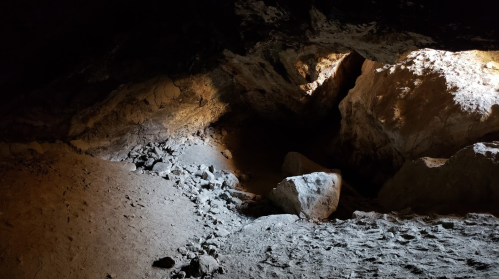 A dimly lit cave interior with rocky terrain and a small opening revealing light.