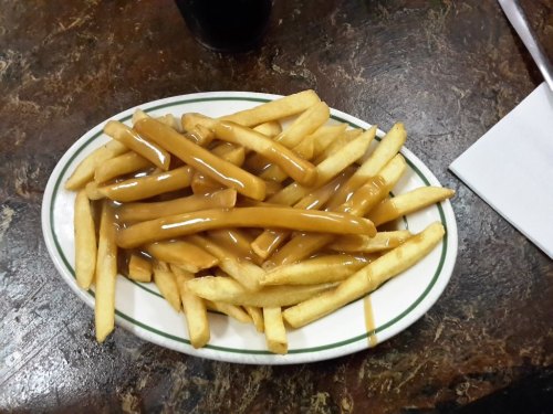 A plate of French fries topped with a generous serving of gravy on a dark table.