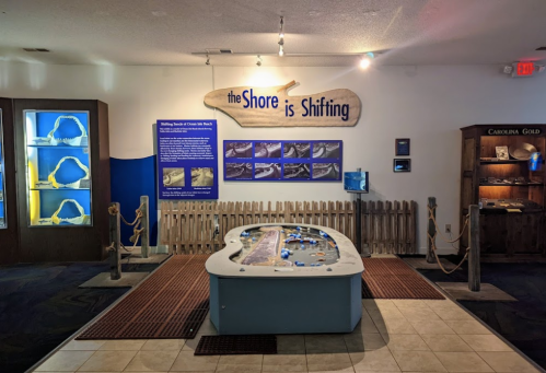Exhibit titled "The Shore is Shifting" with interactive display and informational panels in a museum setting.
