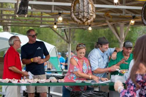 A group of five people at a food stall, chatting and serving food at an outdoor event under string lights.