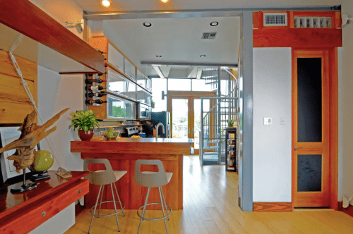 Modern kitchen with wooden accents, bar stools, and a spiral staircase leading to an upper level. Bright and open design.