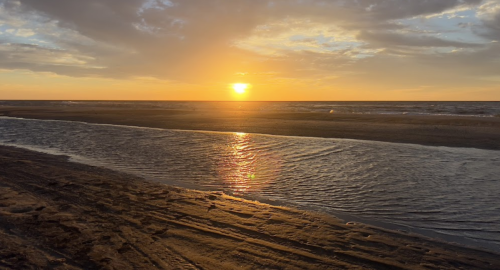 Sunset over a beach, with golden light reflecting on the water and clouds scattered in the sky.
