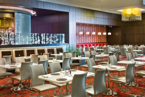 Modern restaurant interior with sleek tables, chairs, and decorative lighting, featuring a vibrant carpet and stylish decor.