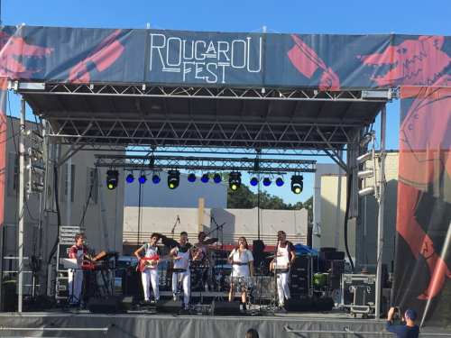A live band performs on stage at Rougarou Fest, with colorful lights and a festive backdrop.