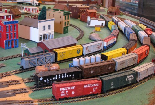 A colorful model train layout featuring various freight cars and buildings on a curved track.