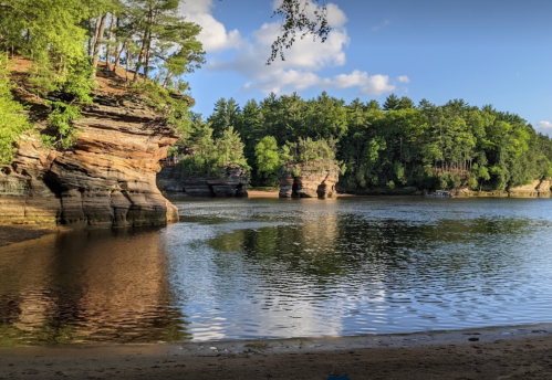 Scenic view of a calm lake surrounded by rocky cliffs and lush green trees under a partly cloudy sky.