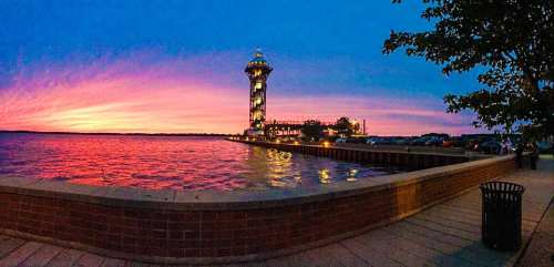 A vibrant sunset over a waterfront with a tall tower and colorful sky, reflecting on the water's surface.