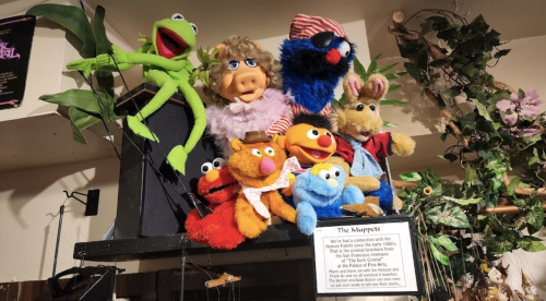 A collection of colorful Muppet characters displayed on a shelf, including Kermit, Miss Piggy, and Elmo.