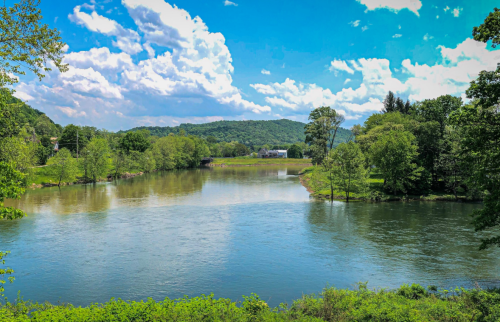 A serene river scene with lush greenery, rolling hills, and a bright blue sky dotted with fluffy clouds.