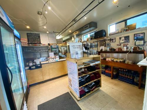 Interior of a cozy café with a counter, shelves of merchandise, and a display fridge, featuring warm lighting.