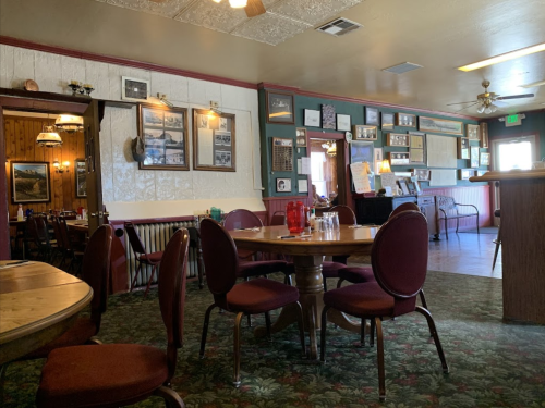 Cozy restaurant interior with round tables, red chairs, and vintage photos on the walls. Warm, inviting atmosphere.
