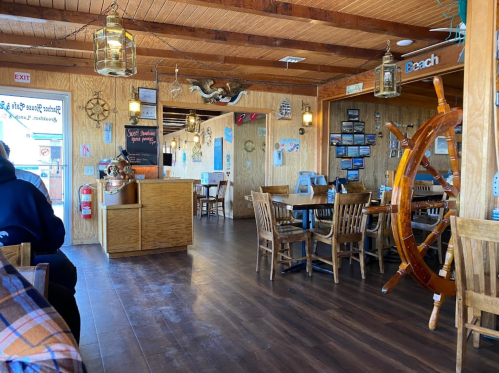 Cozy restaurant interior with wooden decor, nautical themes, and tables set for dining. Warm, inviting atmosphere.