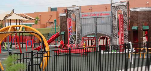 Colorful playground with swings and slides, featuring a ticket booth and decorative arches in the background.