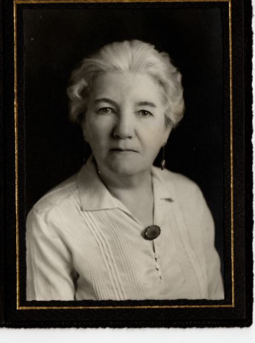 Black and white portrait of a woman with light hair, wearing a collared shirt and a brooch, looking directly at the camera.