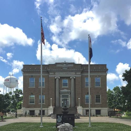 Historic building with columns, flags, and a water tower in the background under a blue sky with clouds.