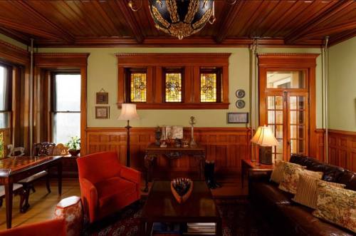 Cozy living room with wooden paneling, stained glass windows, and vintage furniture, featuring orange chairs and a warm ambiance.