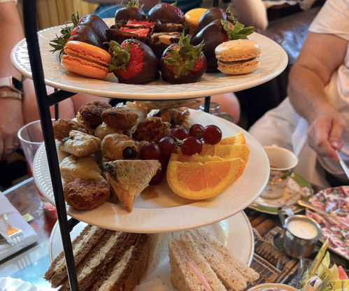 A tiered dessert stand featuring macarons, chocolate-covered strawberries, pastries, and fruit slices.