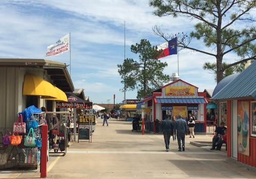 A lively outdoor market with colorful stalls, shoppers, and flags under a blue sky.