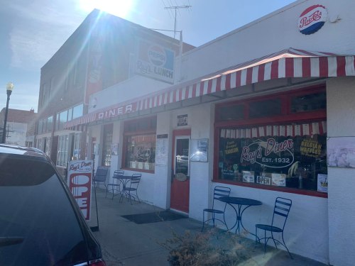 Exterior of Ray's Diner, featuring a red and white striped awning, outdoor seating, and a sign indicating it's open.