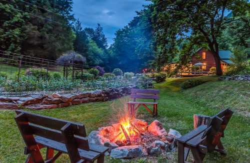 A cozy campfire surrounded by wooden chairs, with a serene garden and cabin in the background under a twilight sky.