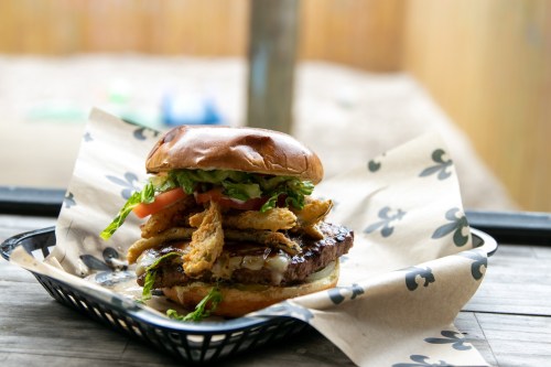 A delicious burger with lettuce, tomato, and crispy fried onions, served on a paper-lined tray.