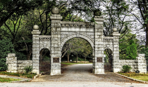 Stone archway entrance with decorative spheres, leading to a tree-lined road.