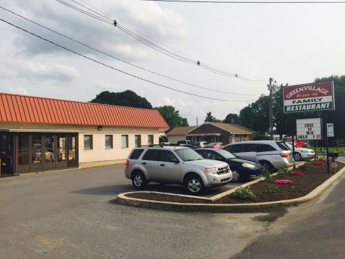 Exterior view of Green Village Family Restaurant with parked cars and a sign, surrounded by greenery and flowers.