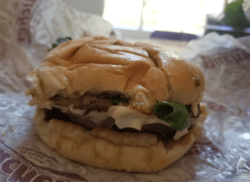 A close-up of a hamburger with lettuce, mayonnaise, and a beef patty, served in a soft bun.