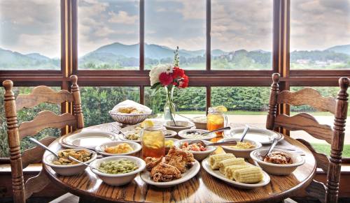 A table set with various dishes, including fried chicken, corn, and sides, with a scenic mountain view through the window.