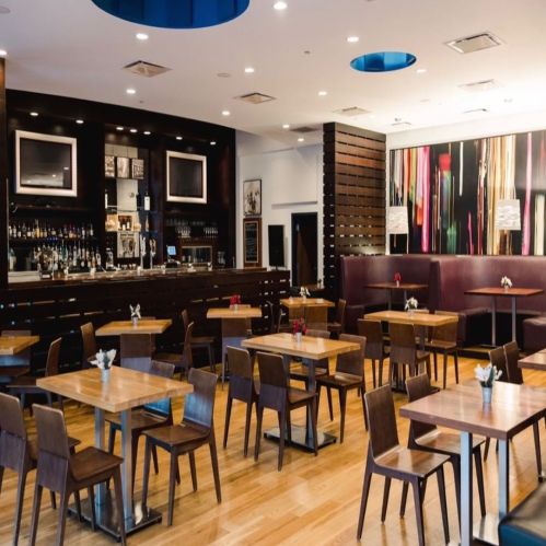 Modern restaurant interior with wooden tables, chairs, a bar, and colorful artwork on the walls.