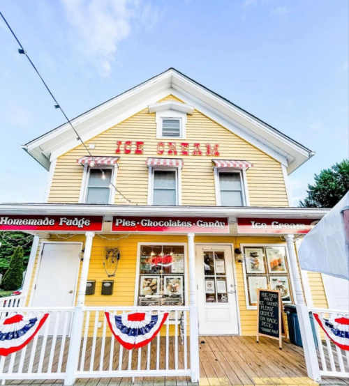 A charming yellow ice cream shop with red and white accents, featuring a porch and patriotic decorations.