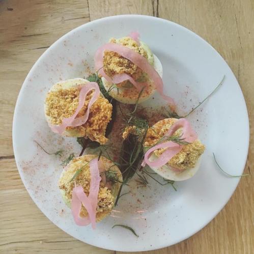 A white plate with four deviled eggs topped with pink pickled onions and herbs, sprinkled with seasoning.