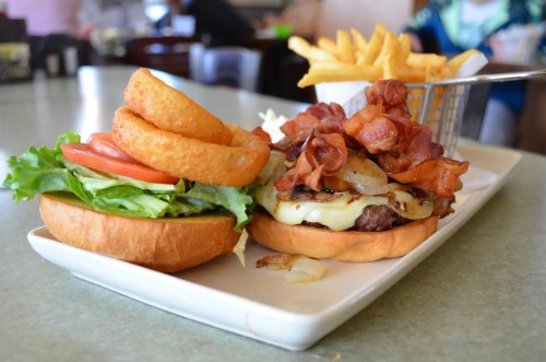 A juicy burger topped with bacon, cheese, and onions, served with onion rings and fries on a plate.