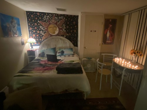 Cozy bedroom with a bed, colorful wall tapestry, candles on a table, and soft lighting.