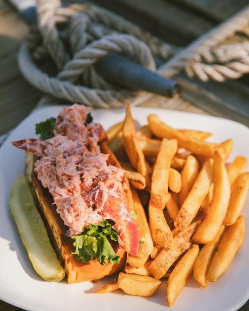 A lobster roll topped with lobster meat and lettuce, served with crispy French fries and a pickle on the side.
