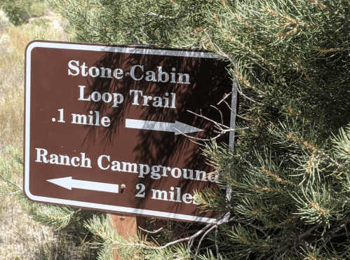 Trail sign indicating directions to Stone Cabin Loop Trail (0.1 miles) and Ranch Campground (2 miles), surrounded by greenery.