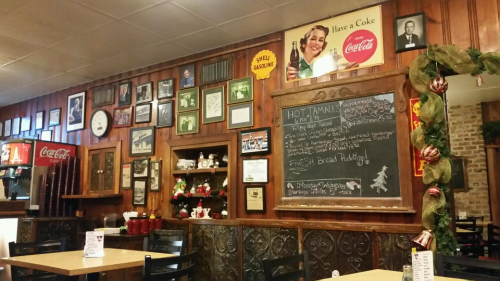 Cozy diner interior with wooden walls, vintage Coca-Cola decor, framed photos, and a chalkboard menu.