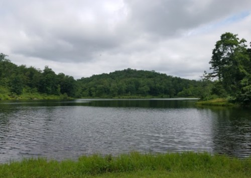 A serene lake surrounded by lush greenery and hills under a cloudy sky.