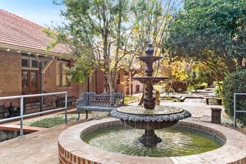 A decorative fountain surrounded by greenery and benches in a serene courtyard setting.