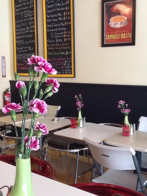 A cozy restaurant interior with tables, chairs, and pink flowers in vases, featuring a menu board on the wall.