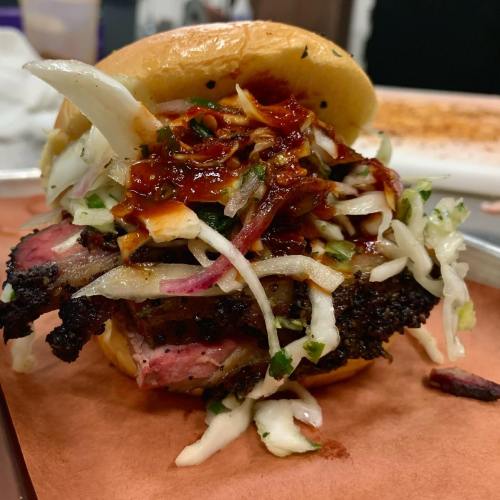 A close-up of a barbecue sandwich filled with smoked meat, coleslaw, and barbecue sauce on a soft bun.