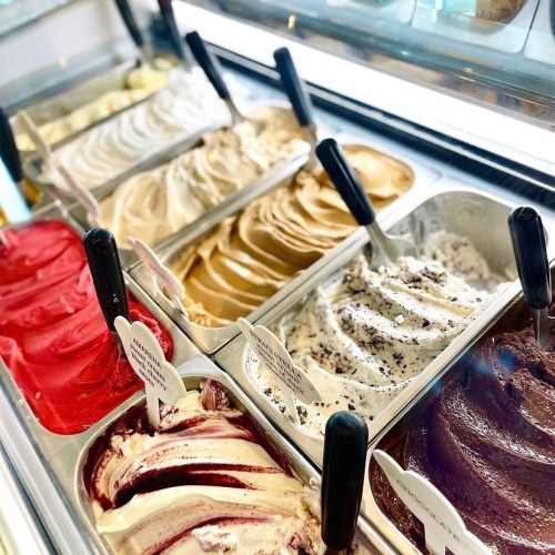 A variety of colorful gelato flavors displayed in metal containers with black scoops.