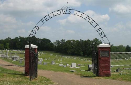 Archway entrance to Odd Fellows Cemetery, with gravestones visible in the background under a cloudy sky.