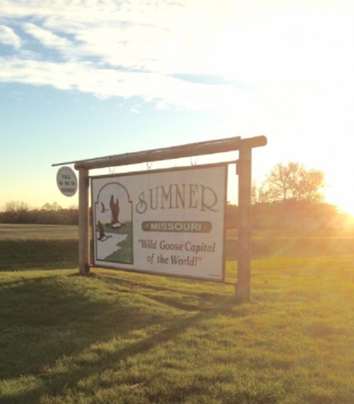 Sign for Sumner, Missouri, reading "Wild Goose Capital of the World," with a sunset in the background.